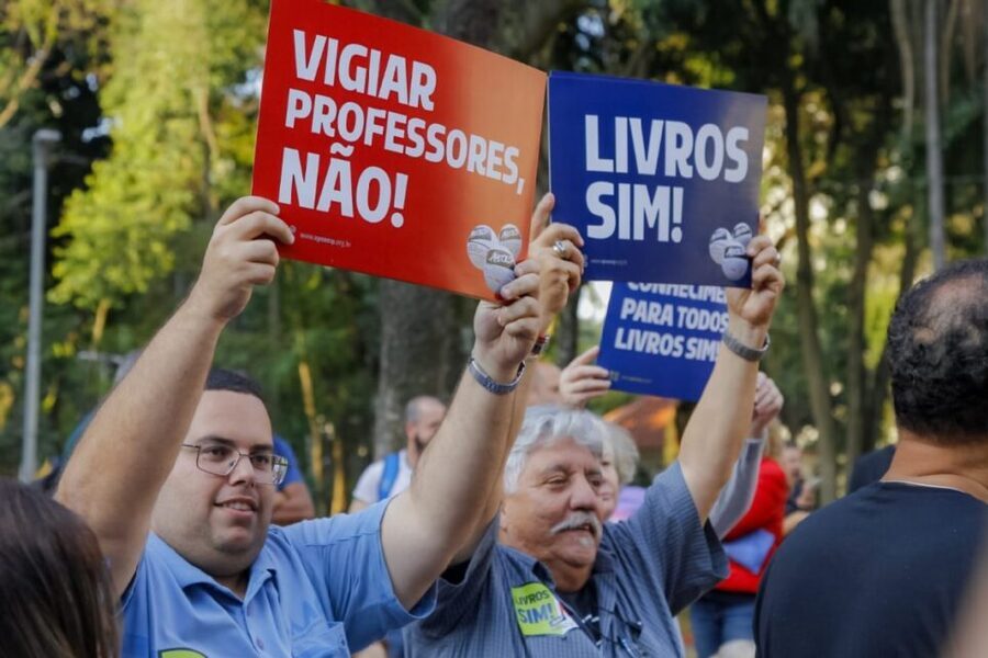 Professores portam cartazes dizendo: "Vigiar professores, não!" e "Livros sim"