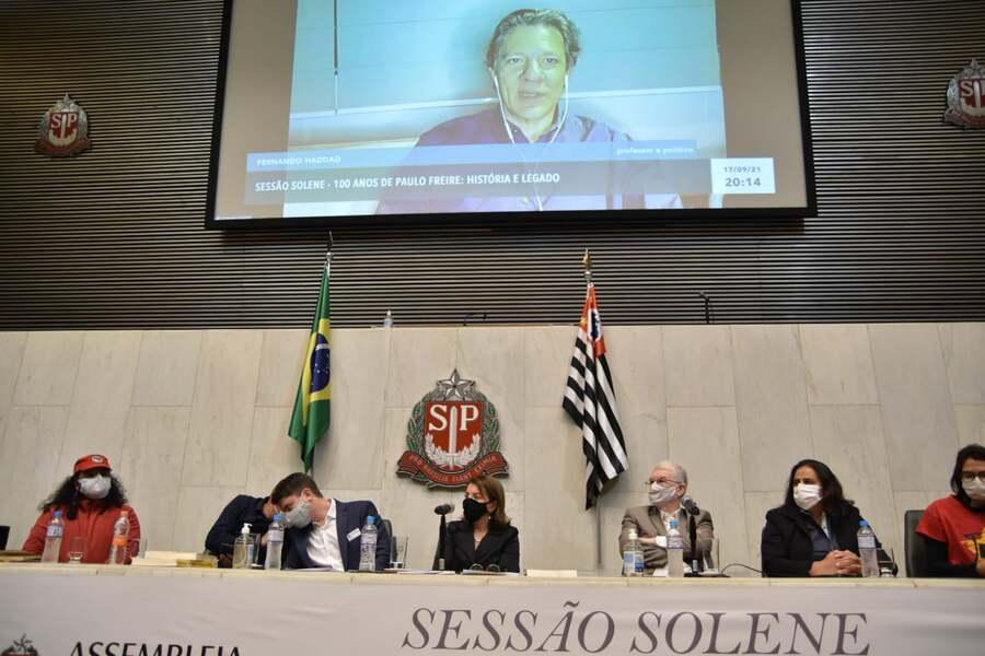 Ato solene na Alesp em homenagem a Paulo Freire. Na mesa, os convidados com Deputada Professora Bebel ao centro. A cima, no telão, vídeo de Fernando Haddad falando.