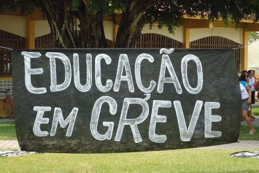 Faixa pregada entre duas árvores em que se lê "Educação em Greve"