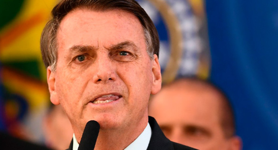 Foto de close de Bolsonaro falando ao microfone com a língua entre os dentes