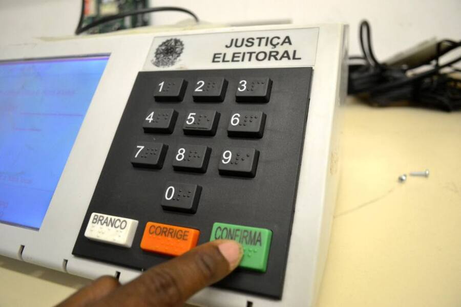 Pessoa aperta tecla da urna de votação