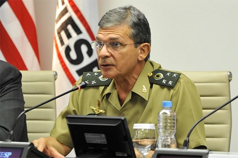 Foto do General Silva e Luna dando entrevista coletiva e falando ao microfone sentado numa mesa