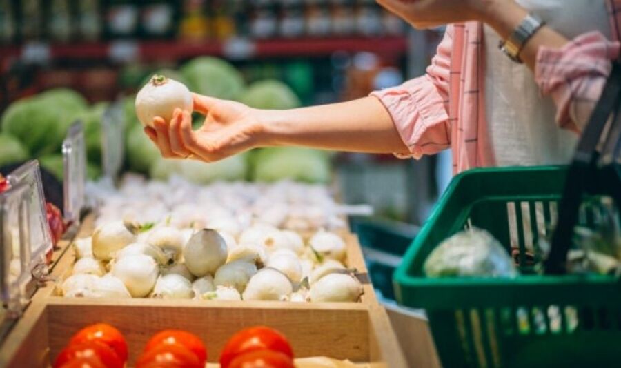 Pessoa observa uma cebola nas mãos diante da gôndola do supermercado