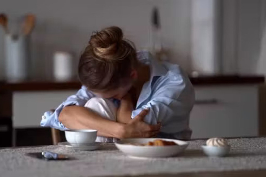 Mulher está sentada à mesa com a cabeça baixa entre os braços