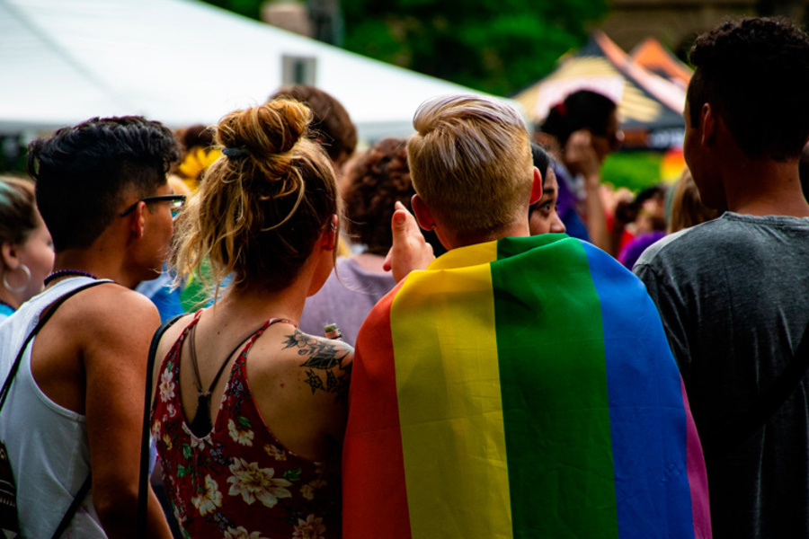 Grupo de jovens LGBTQIAP+, de costas e juntos, assistem a um evento