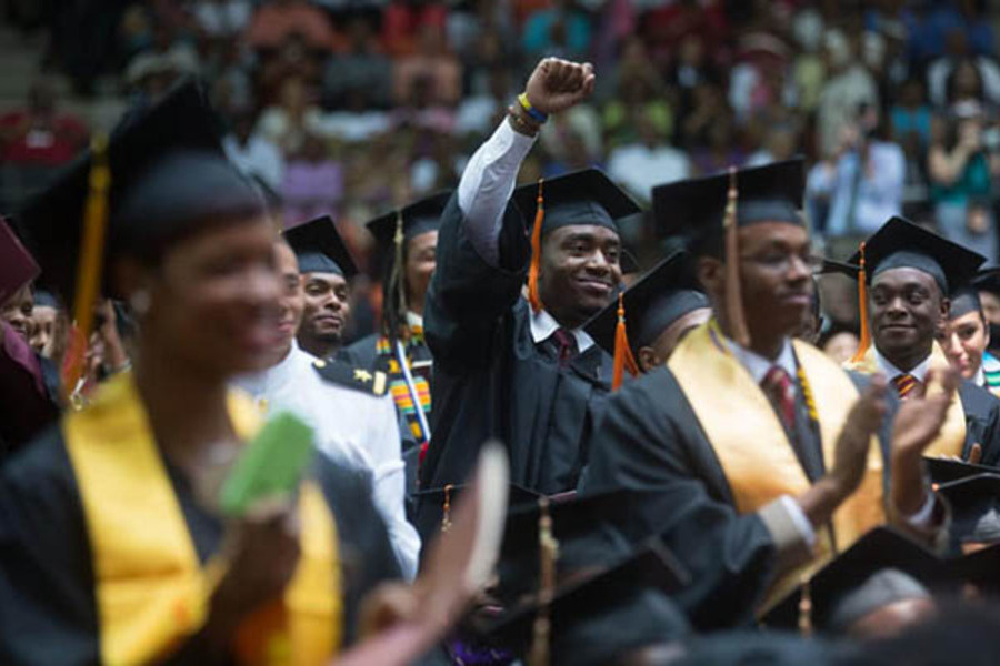 Universitários negros vestidos à caráter na formatura erguem o braço e cerram os punhos