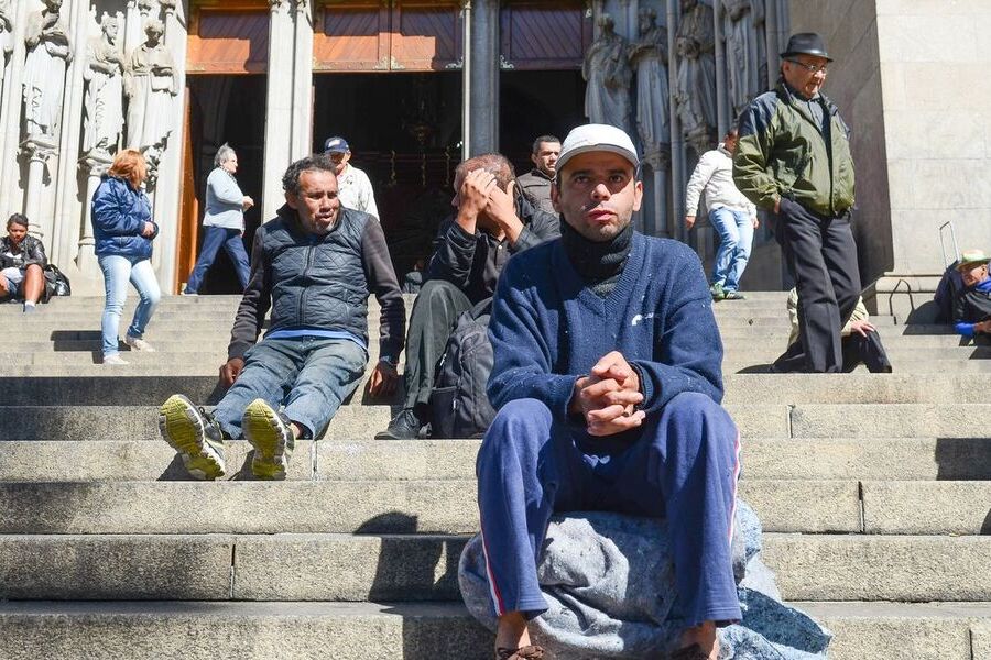 Um grupo de homens e mulheres desempregados sentados nas escadarias da Catedral da Sé.