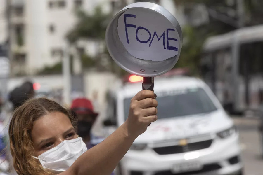 Mulher ergue uma panela vazia com a inscrição "fome"