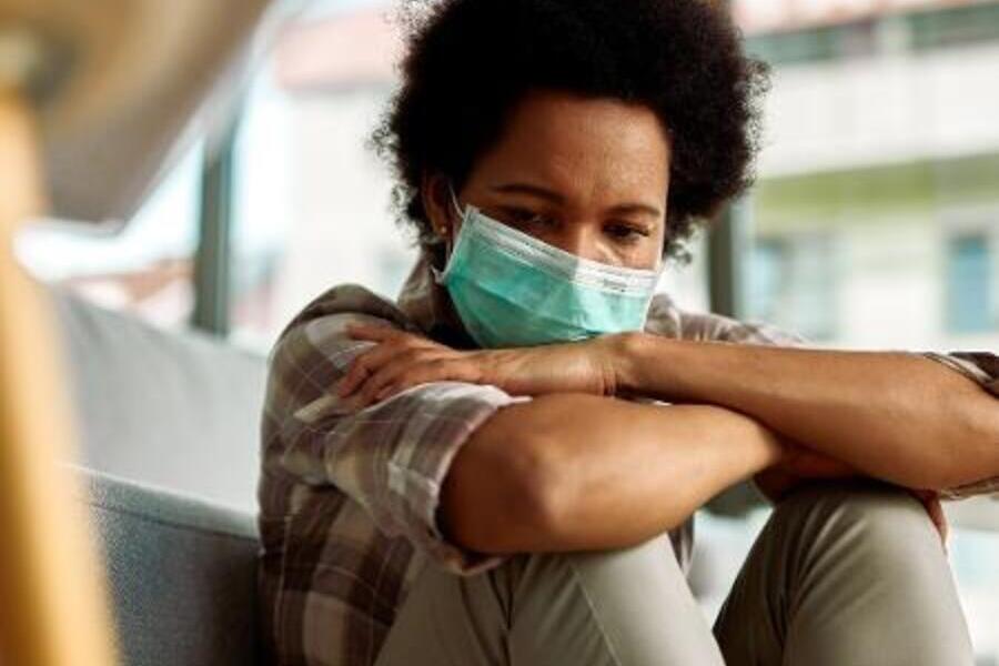 Jovem de máscara e sentado está com as mãos no joelho e de cabeça baixa