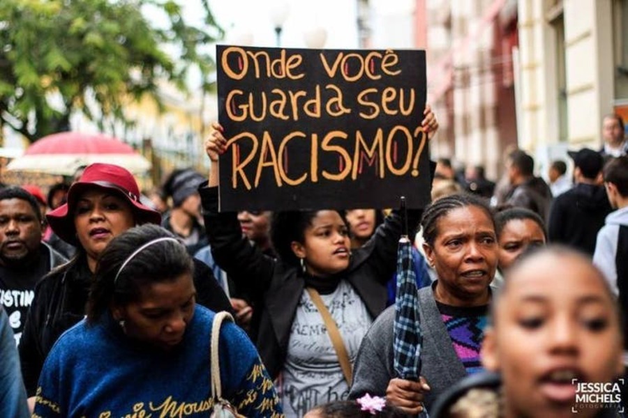 Manifestante no meio da multidão ergue um cartaz com a inscrição: "Onde você guarda o seu racismo?"