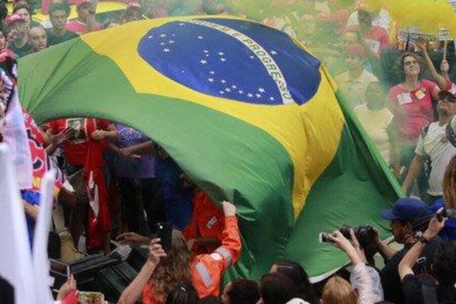 Foto aérea e parcial de uma multidão erguendo a bandeira nacional