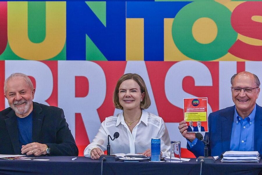 Lula, Gleise Hoffmann e Geraldo Alckmin sentados e sorrindo para as câmeras