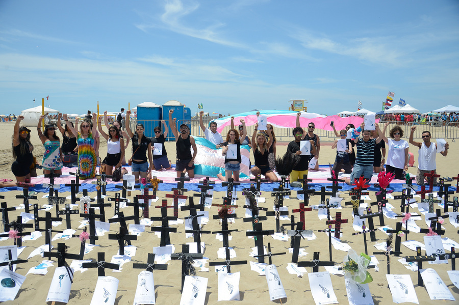 Foto de um protesto em Copacabana no Rio em que várias pessoas erguem cartazes em protesto contra o assassinato de pessoas trans. No chão, inúmeras cruzes fincadas lembrando sepulturas.